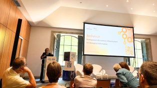 A presenter speaks at the Encontro Ciência 2024 in Porto, discussing BioData.pt, a Portuguese life-science infrastructure for biological information. Audience members listen attentively.